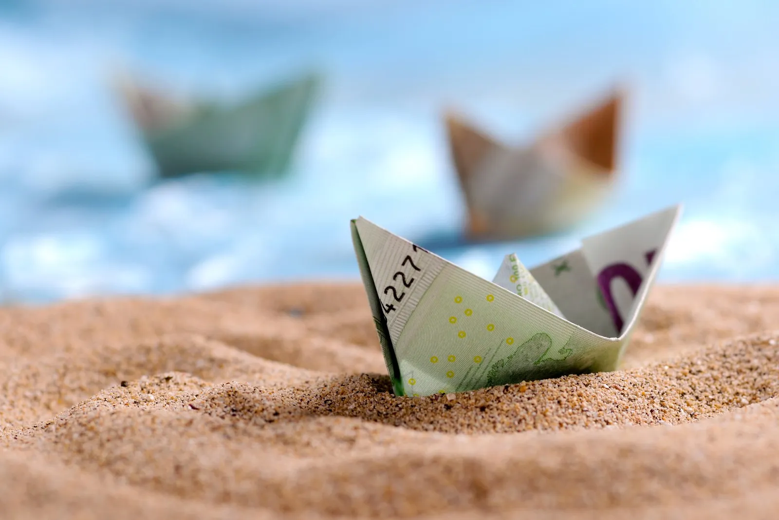 Ein Boot aus einem gefalteten 100-Euro-Schein im Sand.