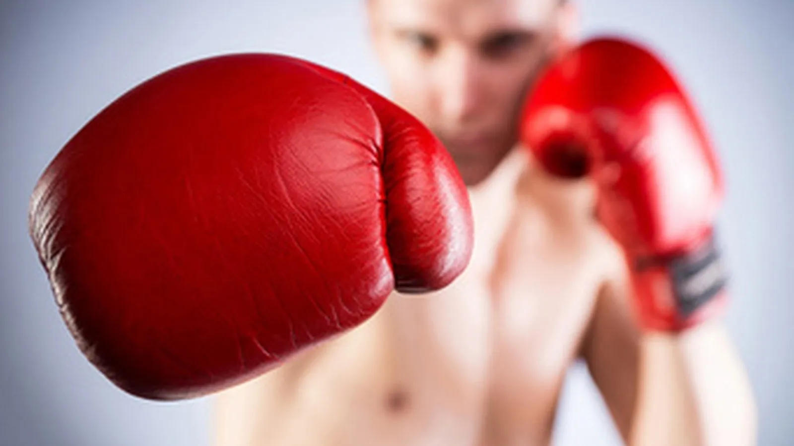 Ein junger Mann mit freiem Oberkörper und roten Boxhandschuhen. Fokus auf die Boxhandschuhe.