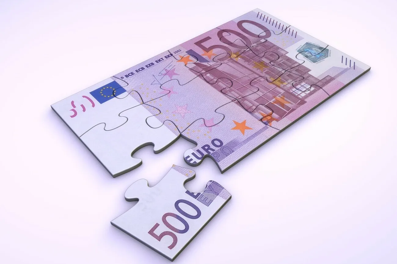 Ein 500 Euro Schein als Puzzle dargestellt, von dem ein Puzzleteil ab ist und daneben liegt.