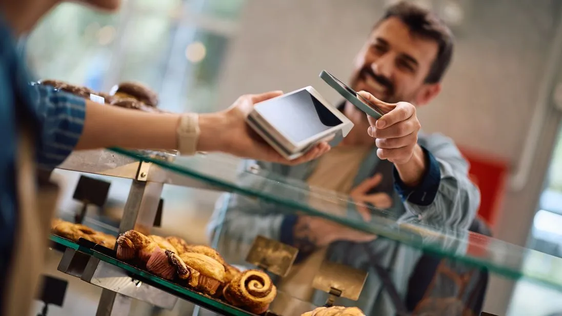ein kunde zahlt per handy in einer bäckerei