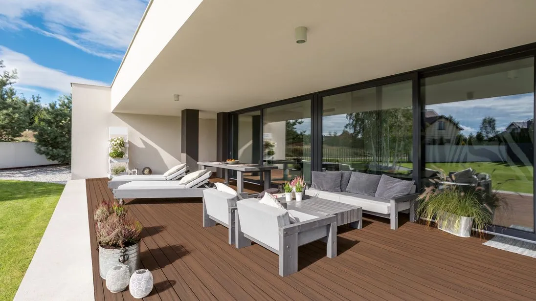 Eine Terrasse mit weißen Möbeln und herbstbraunen Dielen.