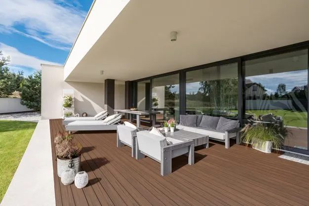 Eine Terrasse mit weißen Möbeln und herbstbraunen Dielen.
