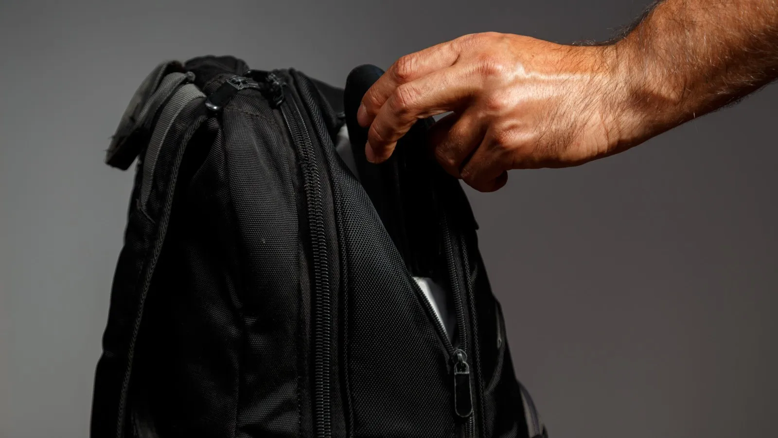 Eine Hand greift nach einem schwarzen Rucksack.