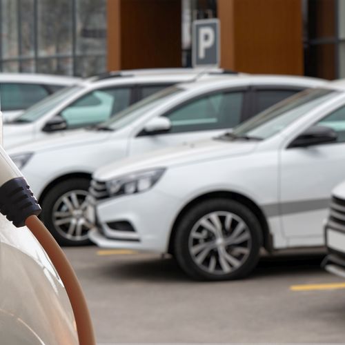 Diverse weiße E-Autos stehen auf einem Parkplatz. Ein Stromer wird gerade geladen.
