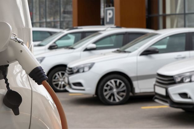 Diverse weiße E-Autos stehen auf einem Parkplatz. Ein Stromer wird gerade geladen.