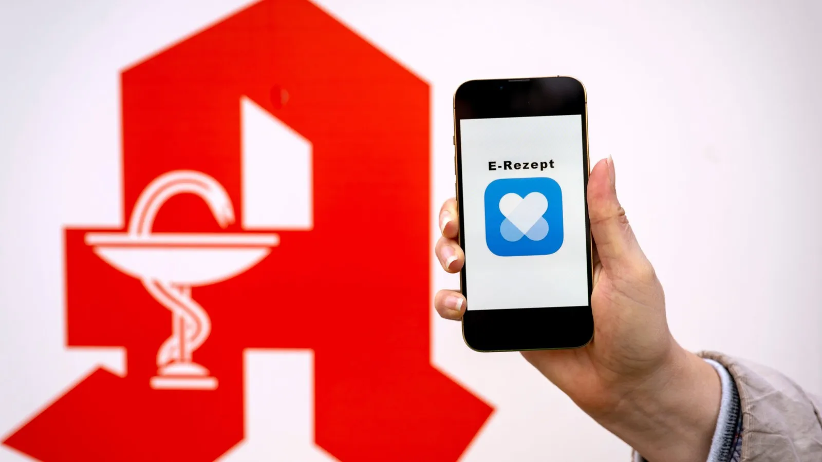 Ein Smartphone wird neben das rote Logo der Apotheke gehalten.