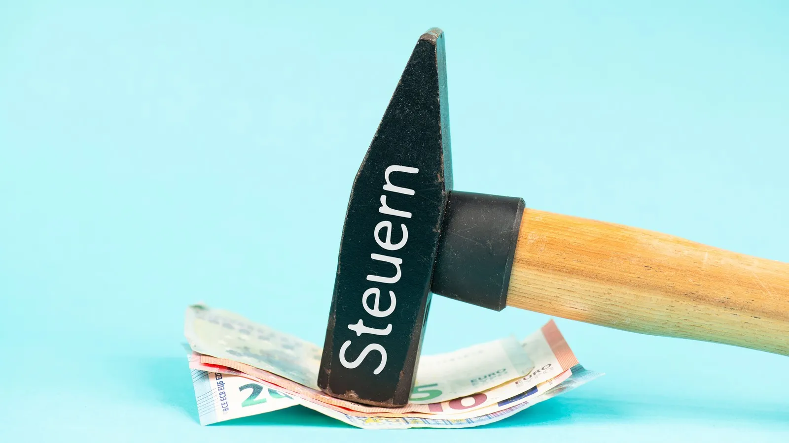 Hammer auf dem das Wort Steuern steht, fixiert ein Bündel Euro-Scheine.