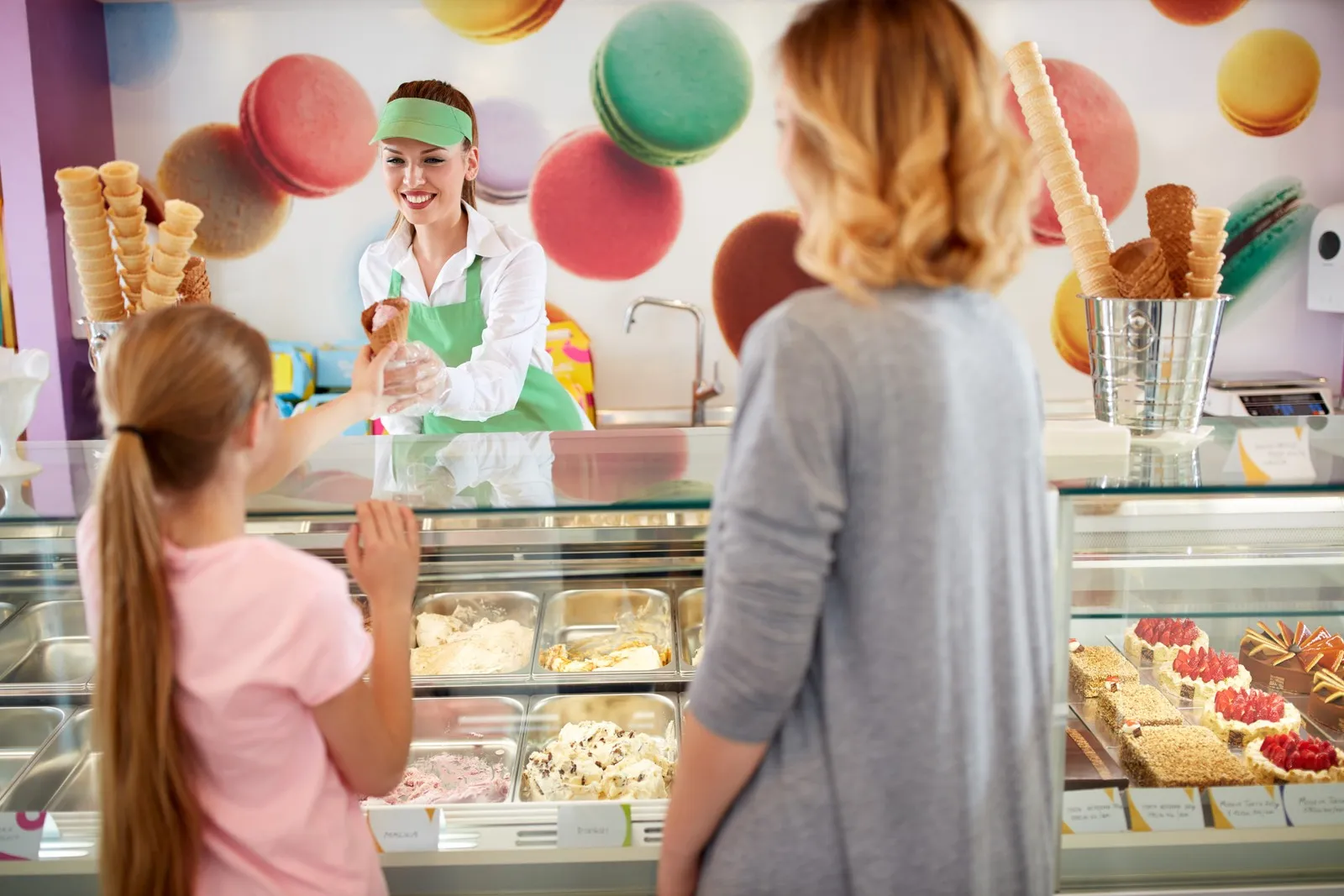 Eine Eisverkäuferin reicht einem Mädchen ein Eis über den Tresen