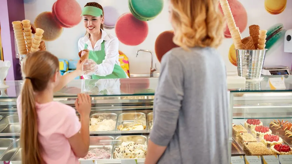 Eine Eisverkäuferin reicht einem Mädchen ein Eis über den Tresen