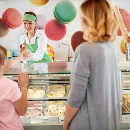 Eine Eisverkäuferin reicht einem Mädchen ein Eis über den Tresen