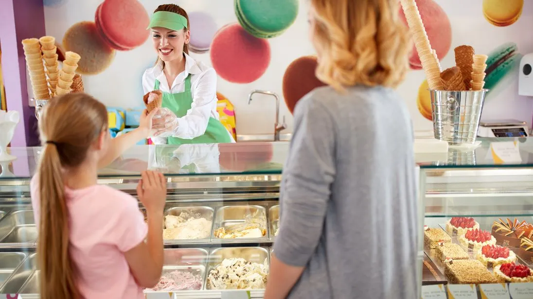 Eine Eisverkäuferin reicht einem Mädchen ein Eis über den Tresen