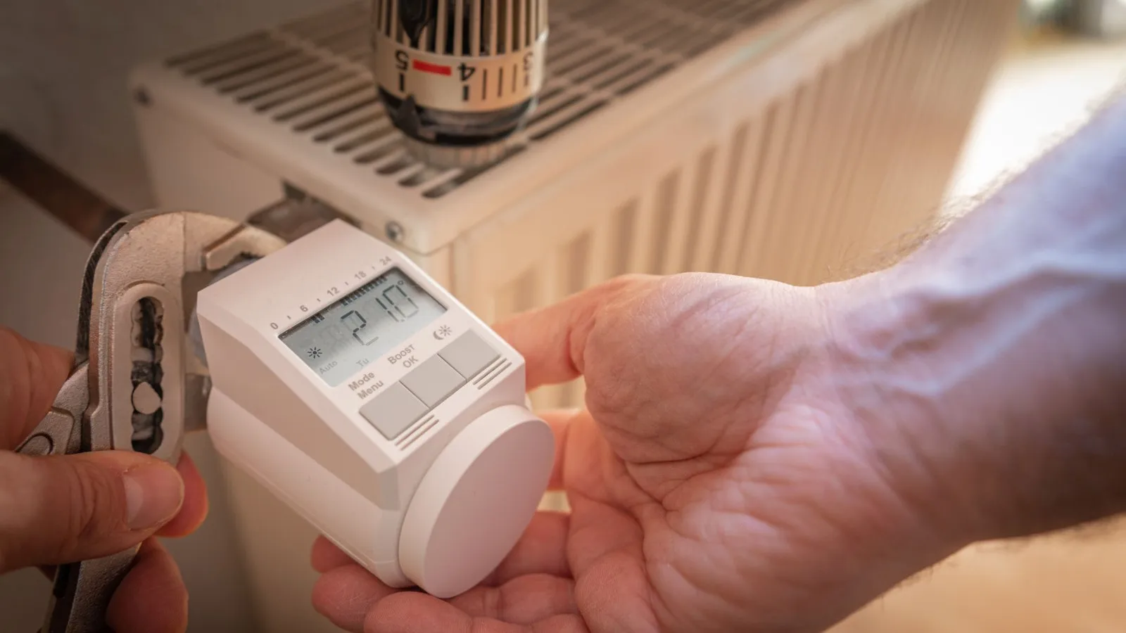 Eine Hand stellt das am Thermostat die Temperatur der Heizung ein.
