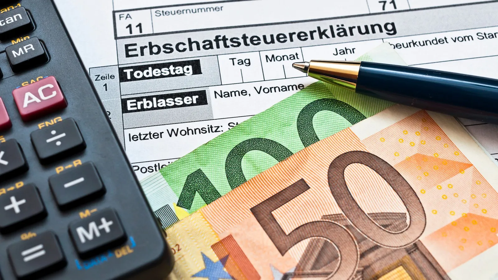 Geldscheine sowie ein Taschenrechner liegen auf einer Erbschaftsteuererklärung