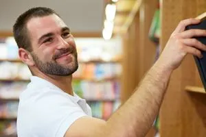 Young man in polo shirt picking a book in a library
