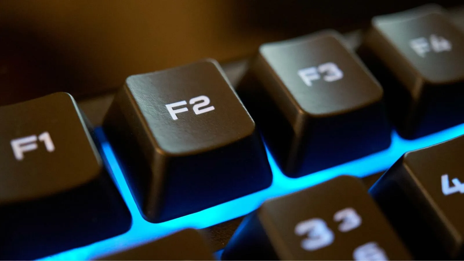 Nahaufnahme der blau beleuchteten F2 Taste einer Computertastatur.