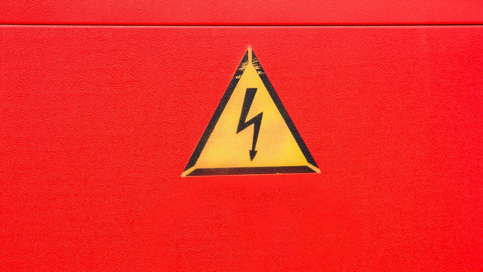 Eine rote Wand auf der ein gelbes Zeichen für Elektrizität gemalt ist.