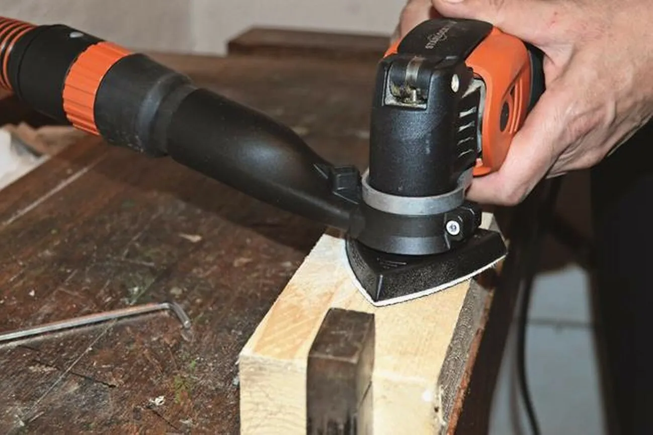 Eine Hand bedient den schwarz orangenen Fein-Oszillierer an einem Holzblock.