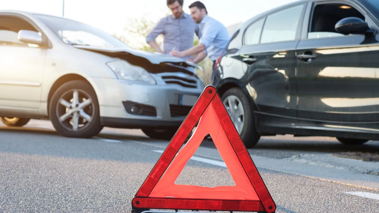 Zwei Männer bei einem Verkehrsunfall mit zwei Autos. Im Fokus steht das Warndreieck.