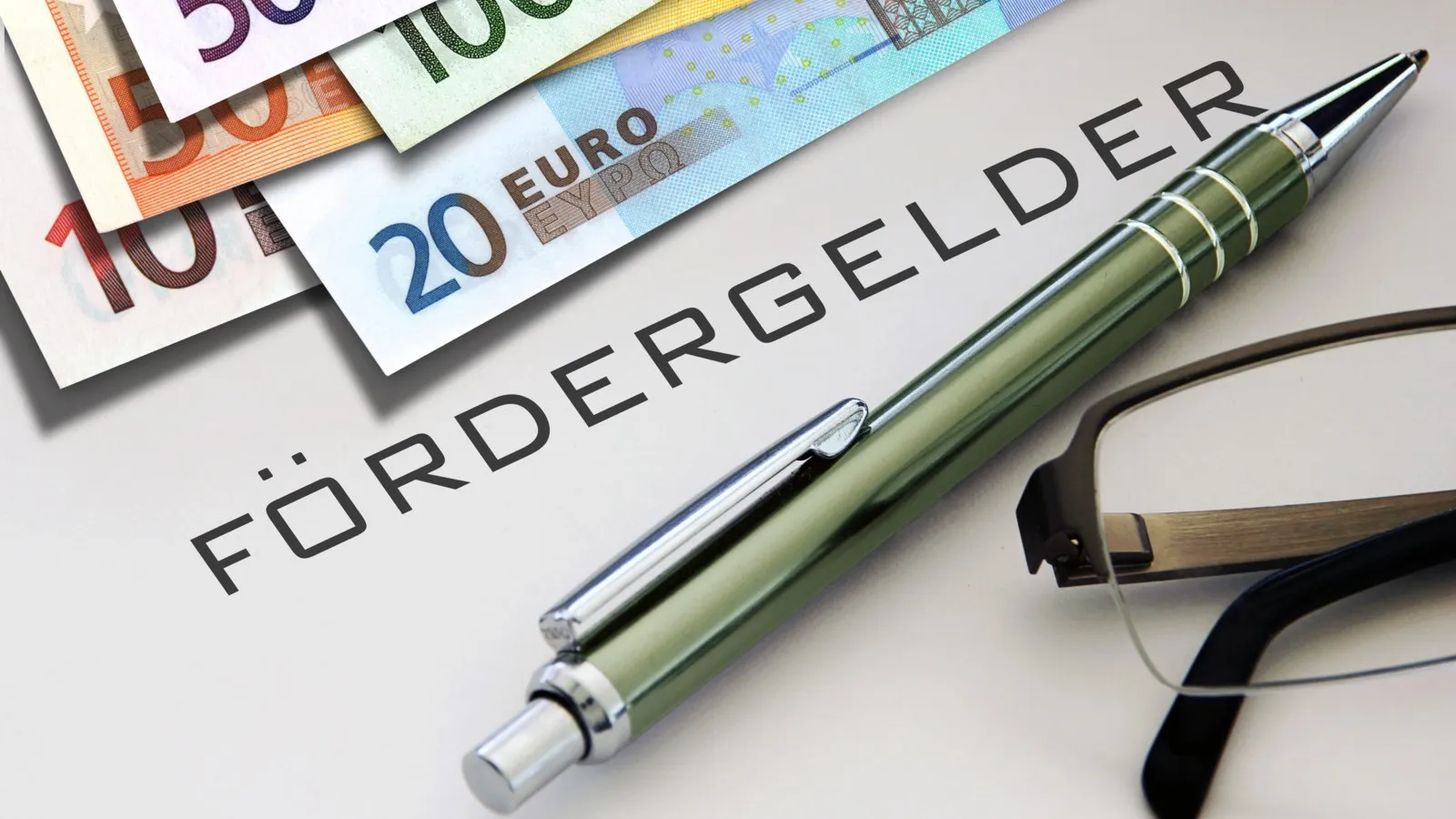 Ein Zettel mit der Aufschrift "Fördergelder", darauf liegen ein grüner Kugelschreiber und mehrere Euro-Scheine.