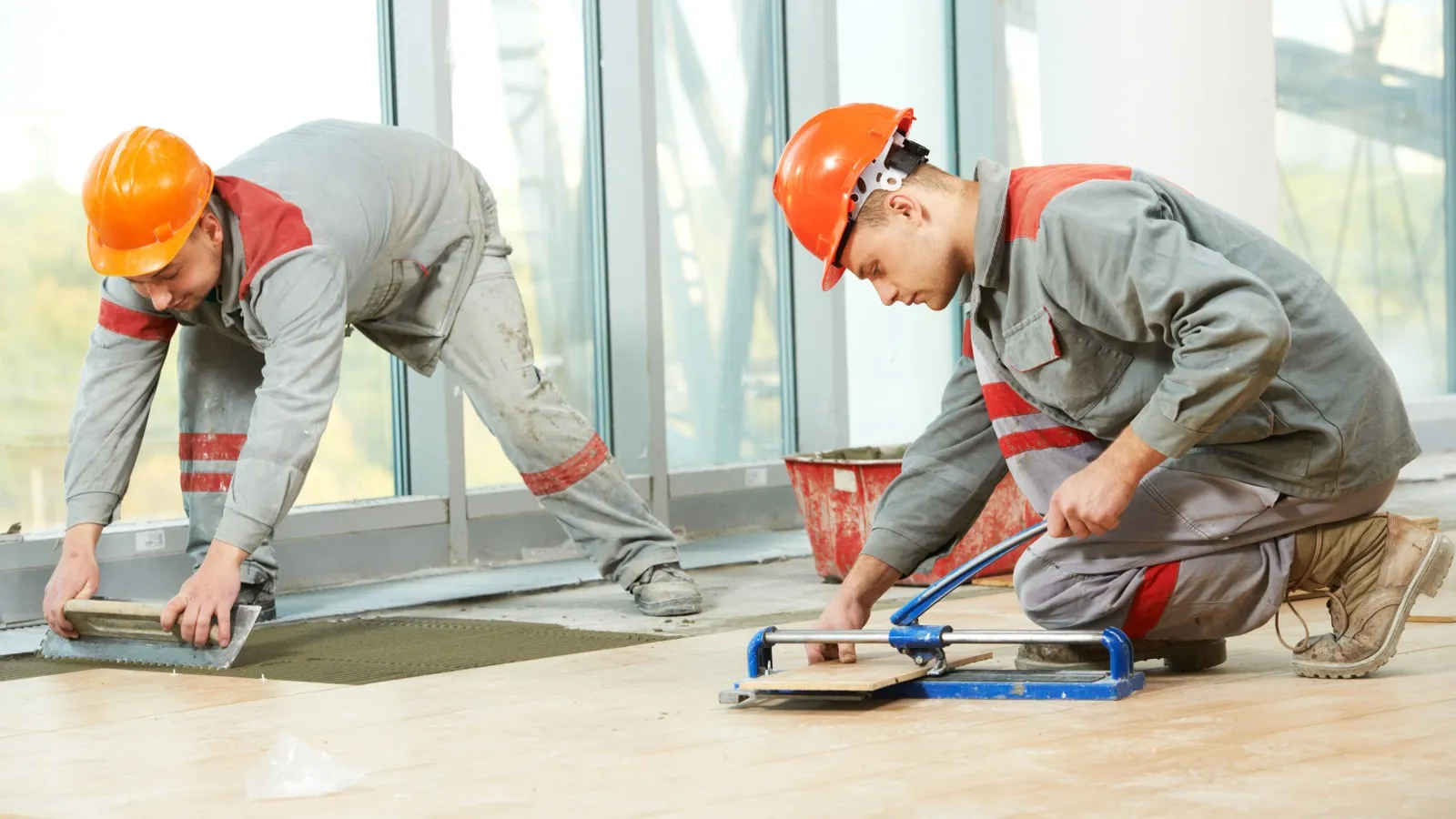 Zwei Handwerker in Arbeitskleidung und orangenen Schutzhelmen verlegen neues Laminat.