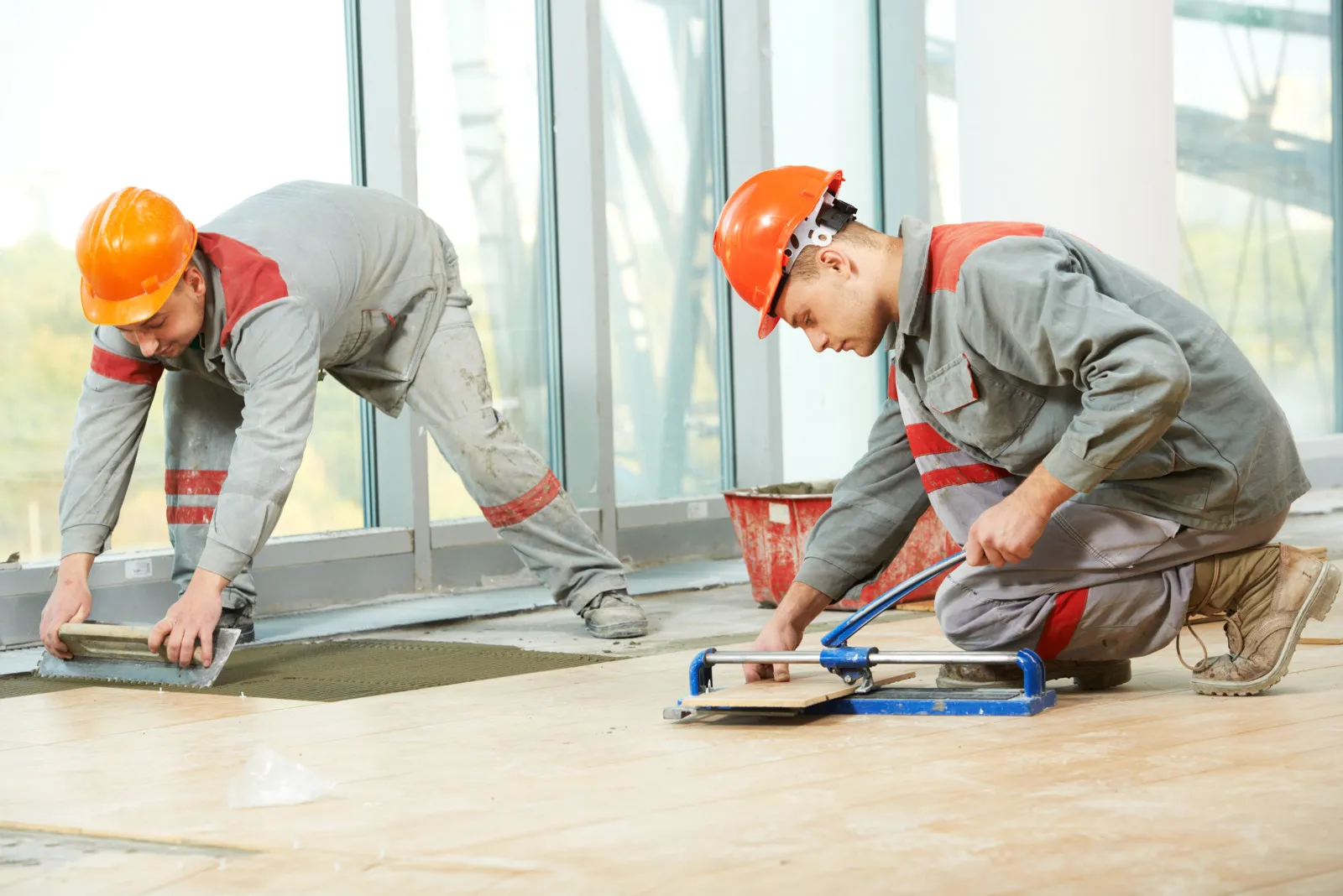 Zwei Handwerker in Arbeitskleidung und orangenen Schutzhelmen verlegen neues Laminat.