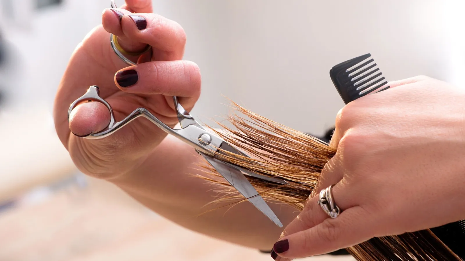 Hände schneiden Haarspitzen mit einer silbernen Schere in der einen Hand und einem Kamm in der anderen.