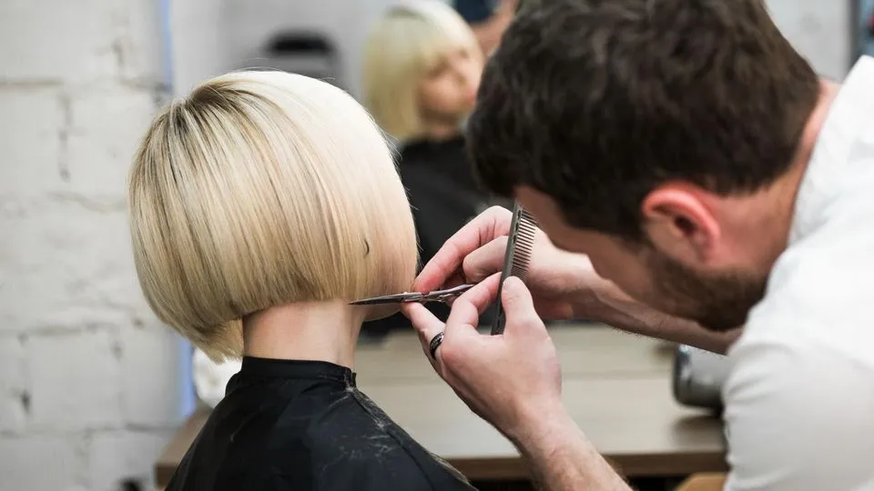 Ein Friseur schneidet einer blonden Frau einen Bob.