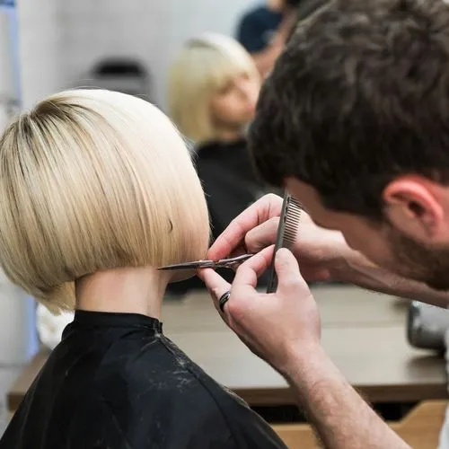 Ein Friseur schneidet einer blonden Frau einen Bob.