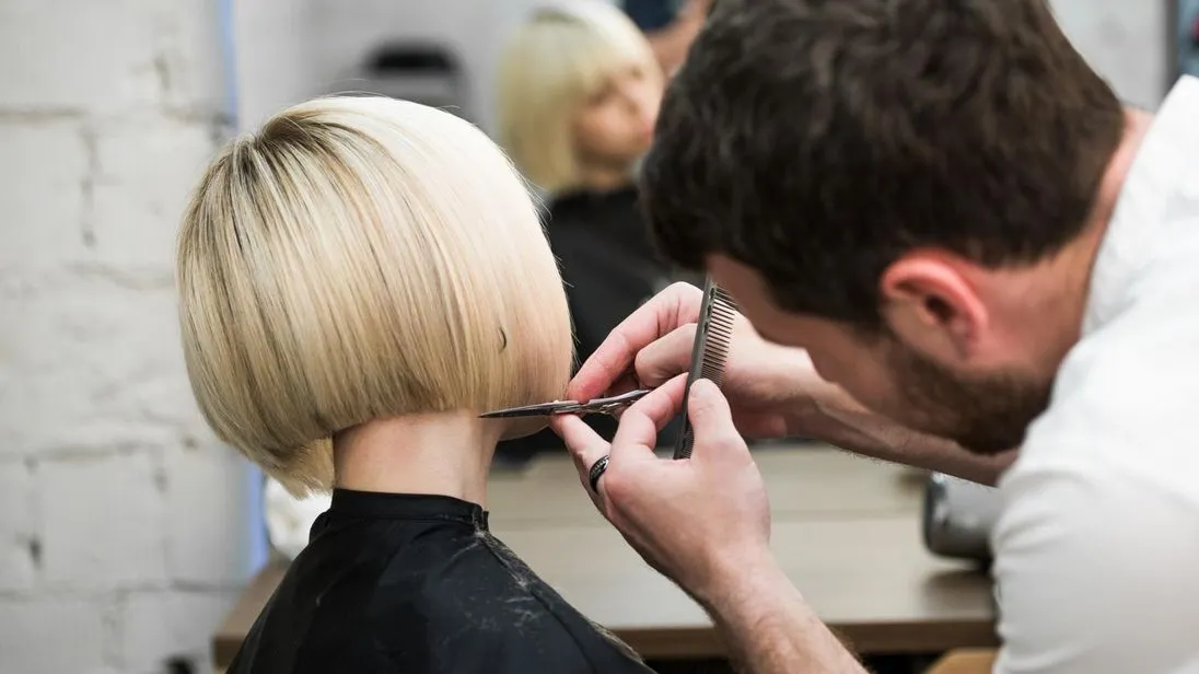 Ein Friseur schneidet einer blonden Frau einen Bob.