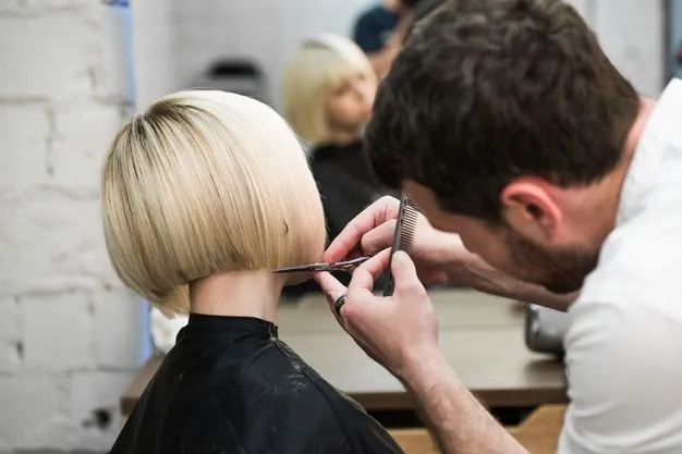 Ein Friseur schneidet einer blonden Frau einen Bob.