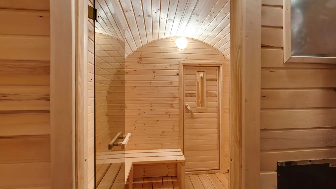 Blick in eine Sauna aus Kieferkolz mit Ofen und Beleuchtung.