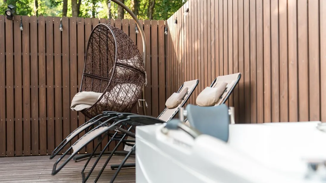 Wellnessbereich in einem Garten mit zwei Liegestühlen, Whirlpool und Holzpalisaden als Sichtschutz.
