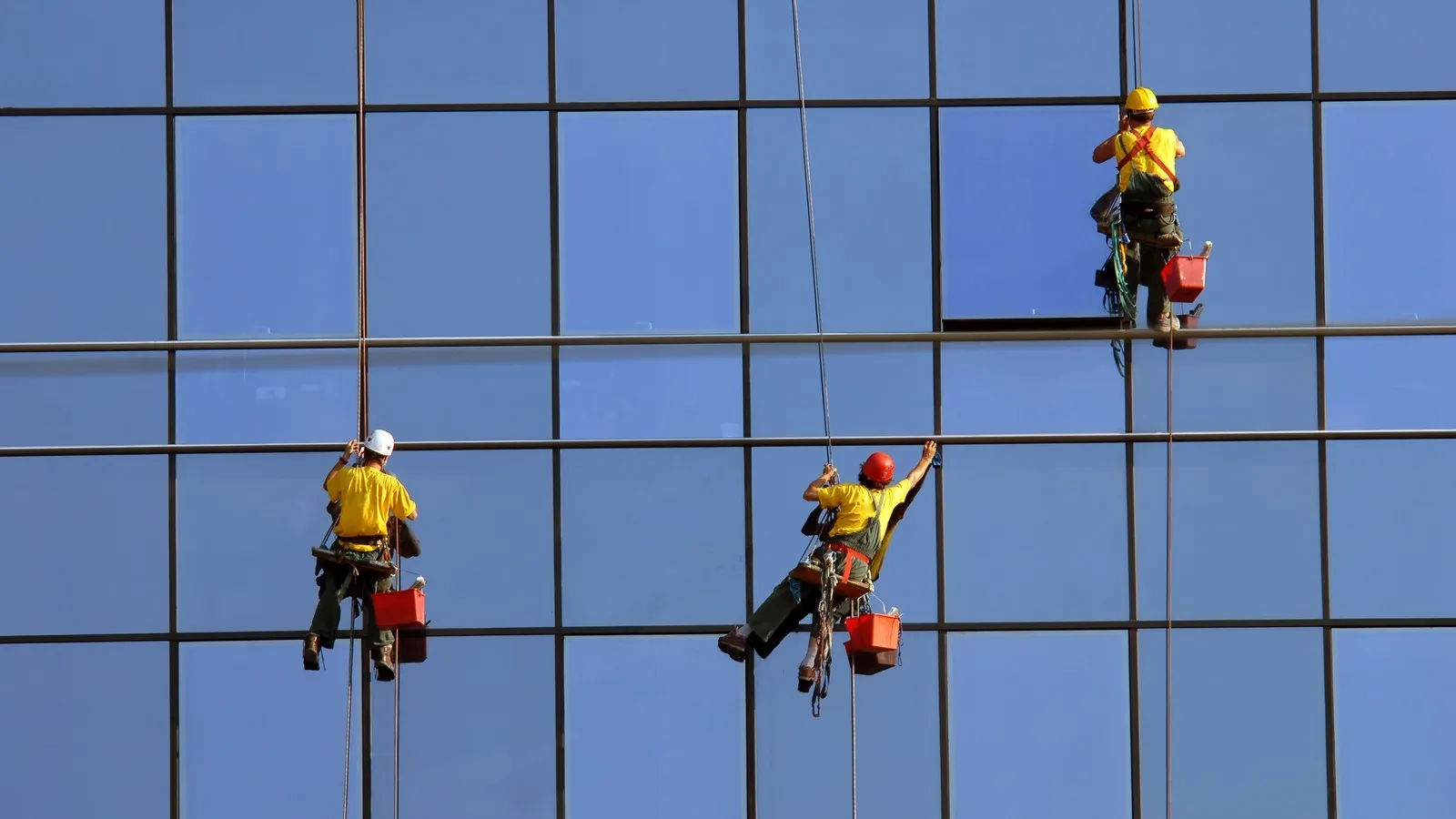 Drei Gebäudereiniger reinigen die Fenster einer Glasfassade