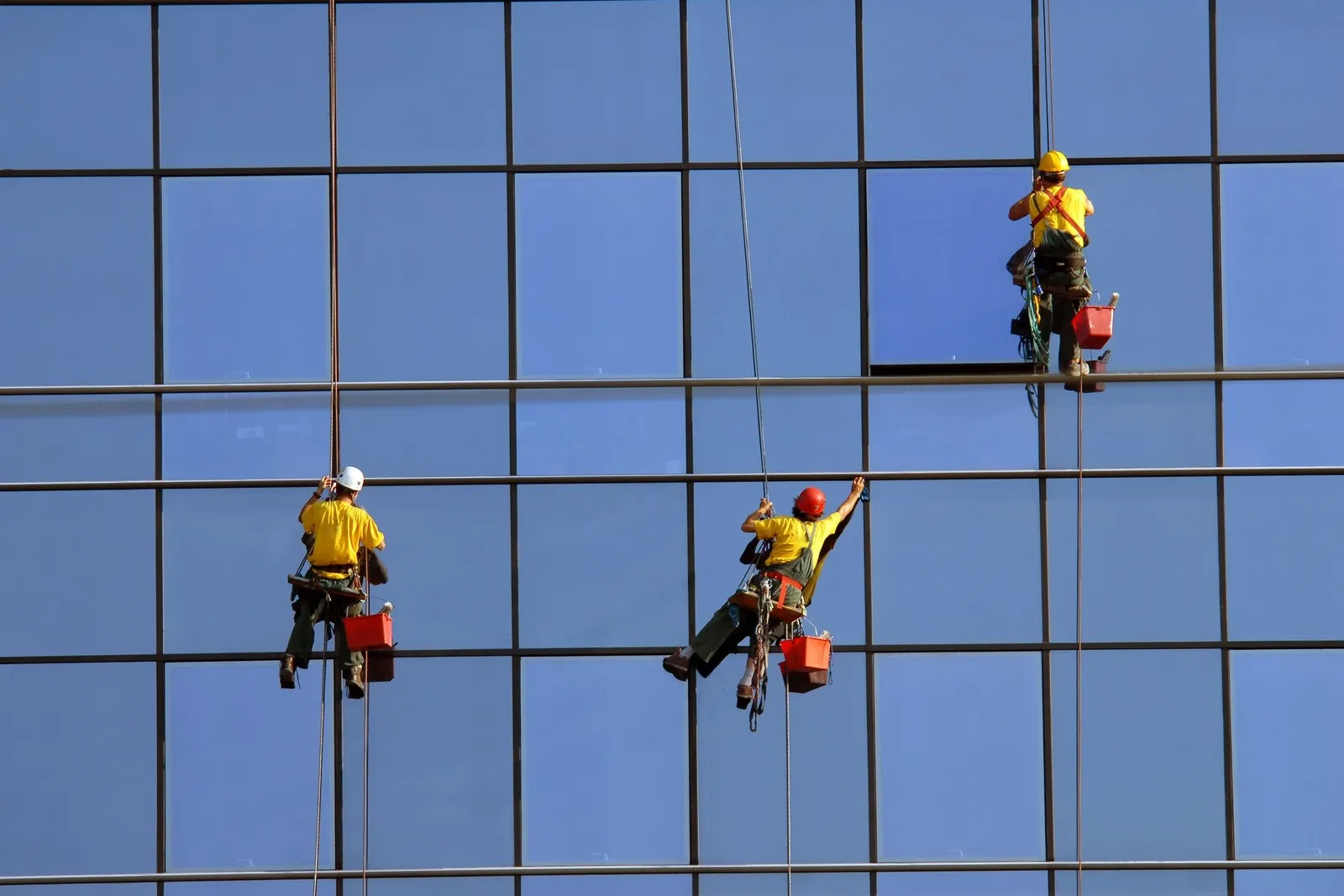 Drei Gebäudereiniger reinigen die Fenster einer Glasfassade