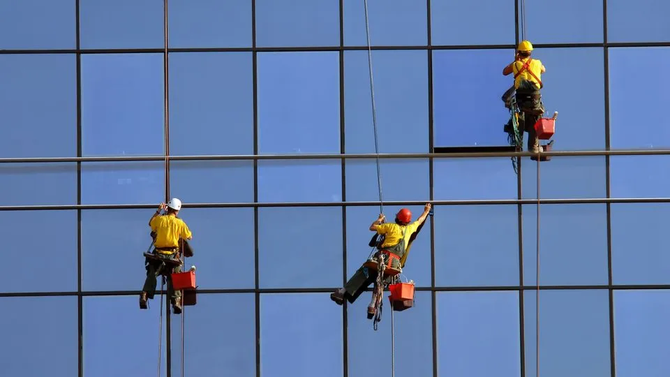 Drei Gebäudereiniger reinigen die Fenster einer Glasfassade