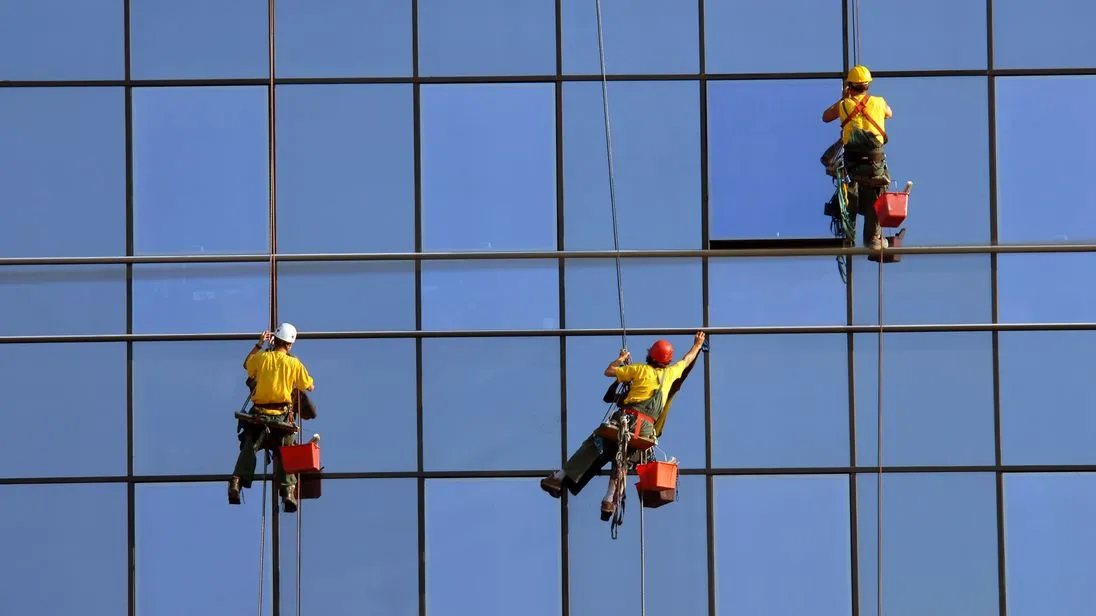 Drei Gebäudereiniger reinigen die Fenster einer Glasfassade