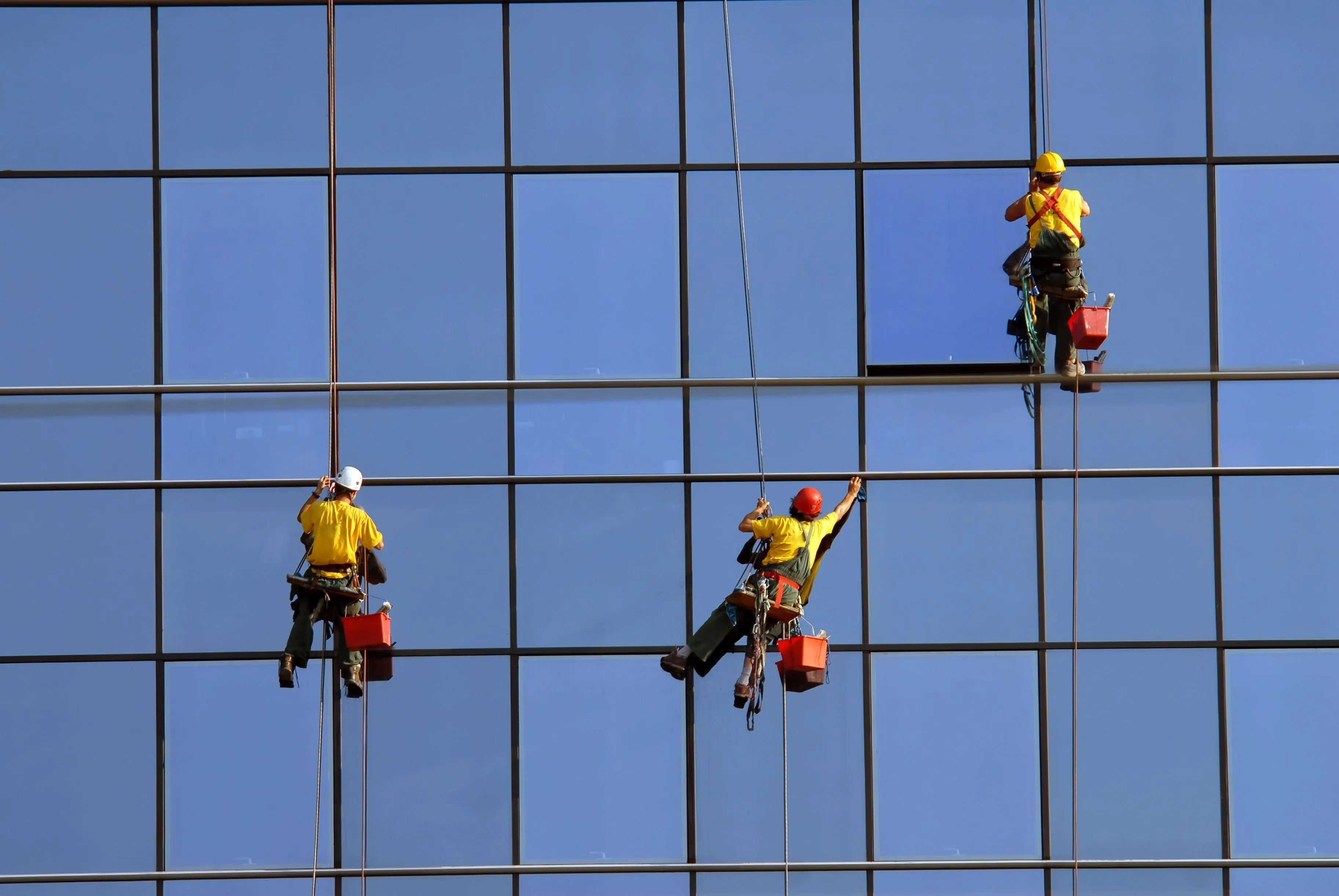 Drei Gebäudereiniger reinigen die Fenster einer Glasfassade