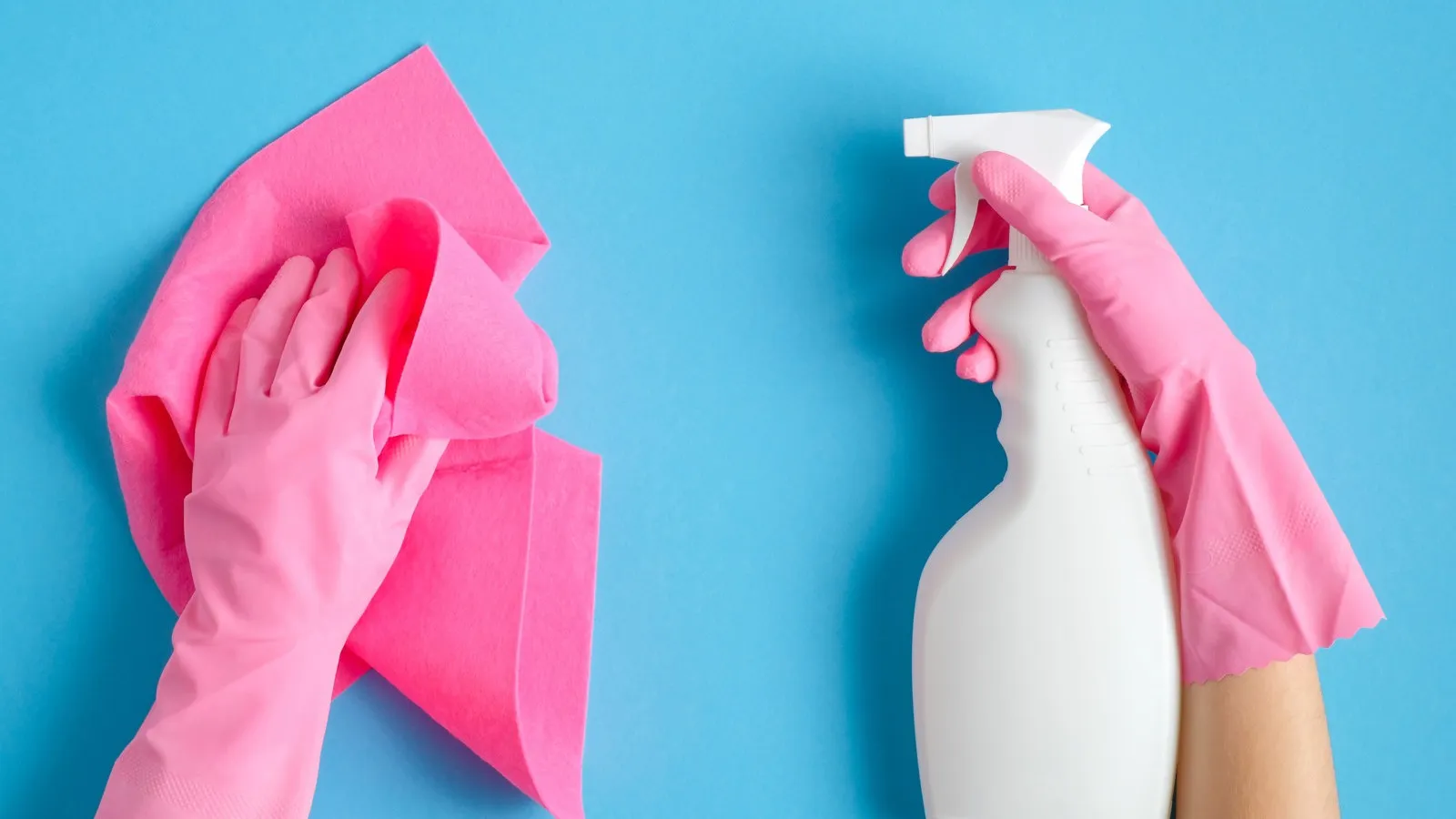 Hände vor einem blauen Hintergrund tragen pinke Handschuhe und halten eine weiße Sprühflasche und ein pinkes Tuch.