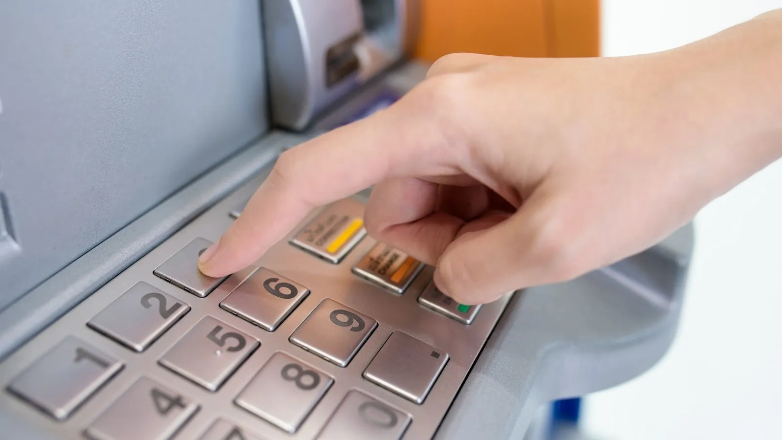 Eine Hand gibt am Bankautomaten eine PIN-Nummer ein, um Geld abzuheben.