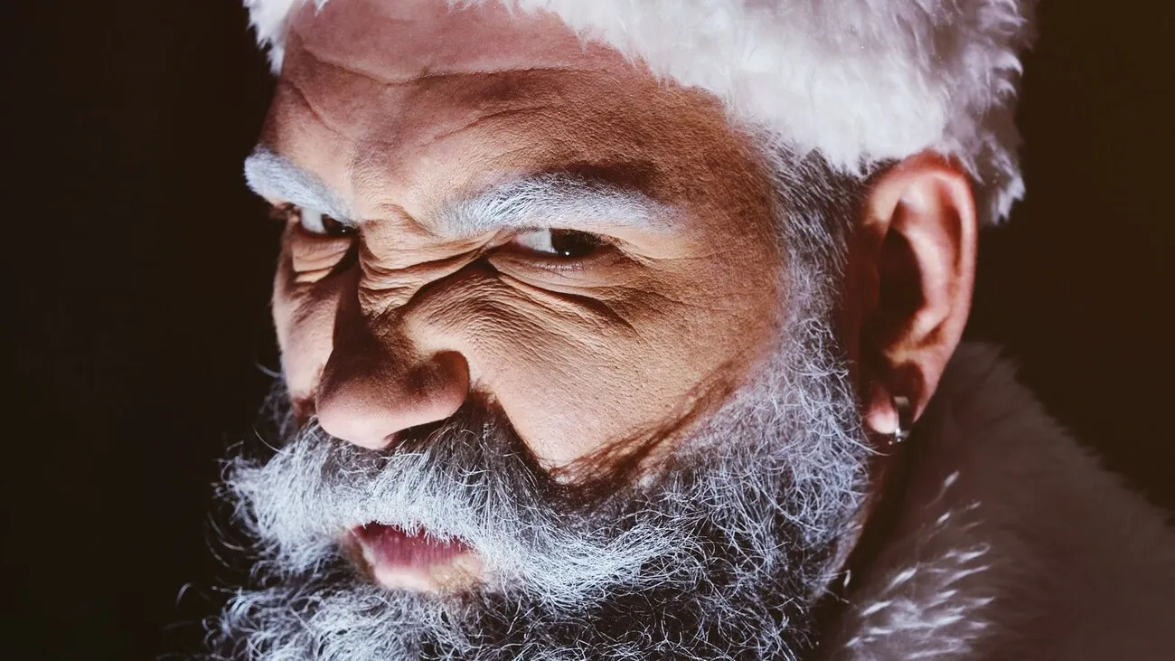 Wütender Weihnachtsmann mit grimmigem Gesichtsausdruck vor dunklem Hintergrund.