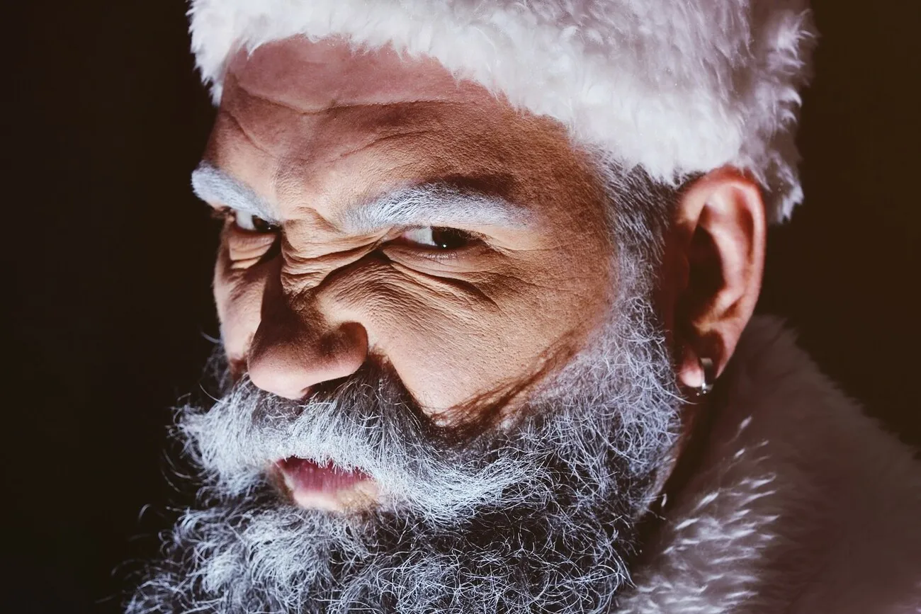 Wütender Weihnachtsmann mit grimmigem Gesichtsausdruck vor dunklem Hintergrund.
