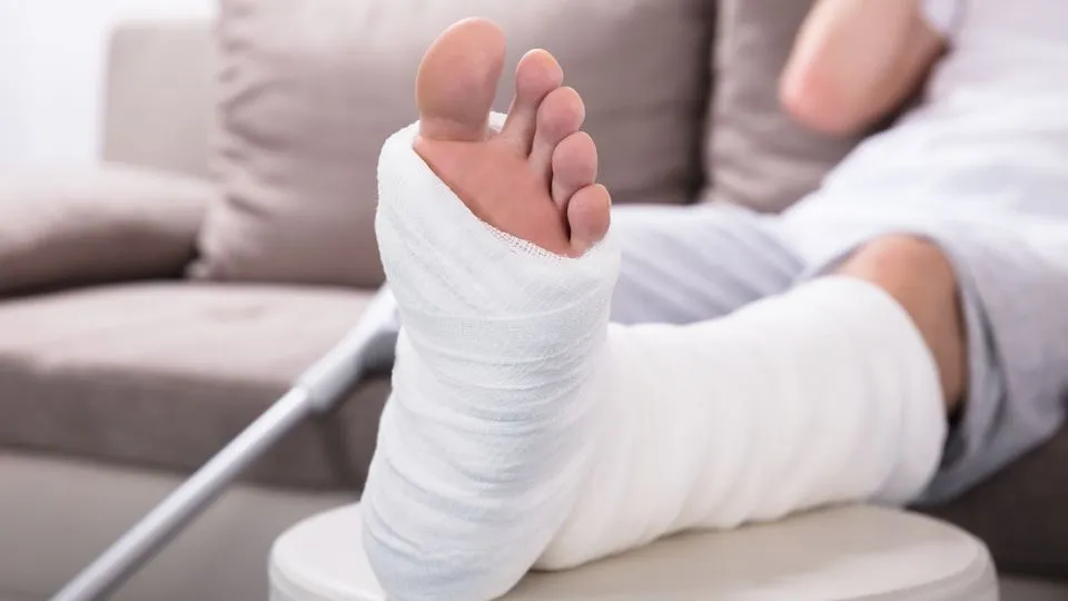 Ein Mann sitzt auf einem Sofa und hat sein gegipstes Bein hochgelegt.