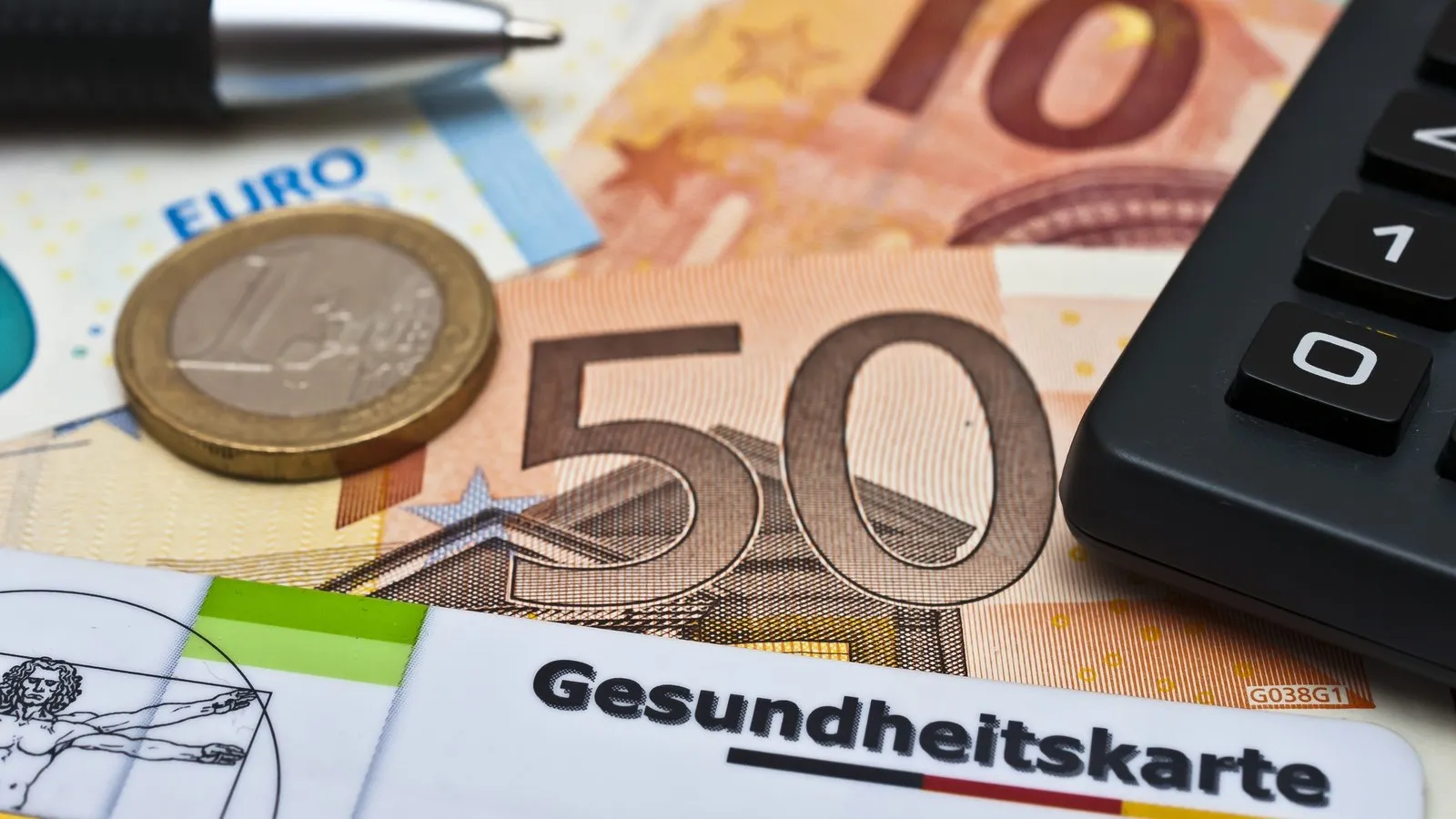 Eine Gesundheitskarte, ein Taschenrechner, ein Kugelschreiber und Geld liegen auf einem Schreibtisch.