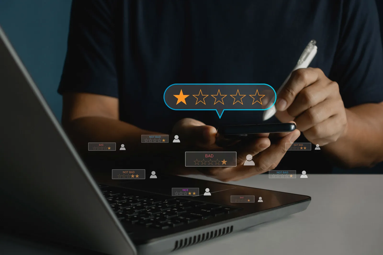 Eine Person arbeitet an einem Laptop und bedient mit einem Stift ein Smartphone. Über dem Display ist eine Sternebewertung zu sehen, bei der nur ein Stern vergeben wurde.