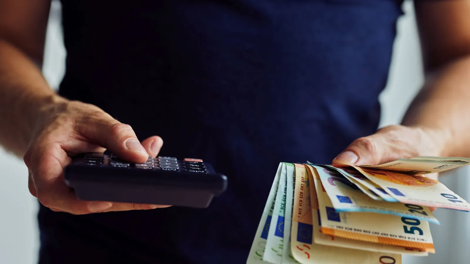 Eine Person hält in der einen Hand einen Taschenrechner und in der anderen mehrere Geldscheine.