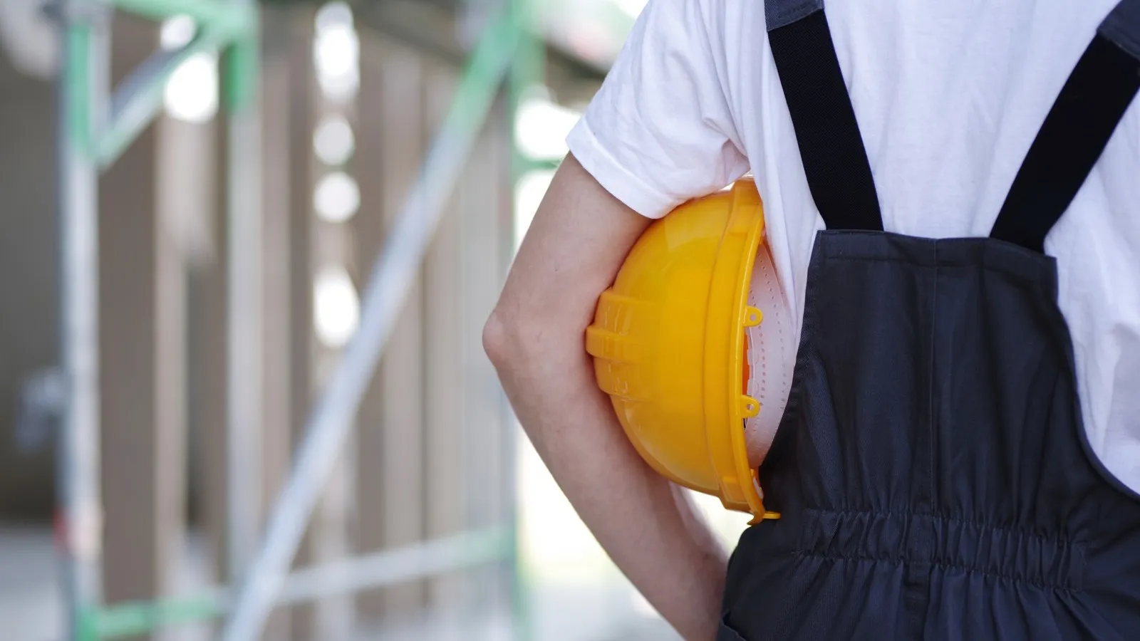 Handwerker im Blaumann hat einen gelben Helm unter den Arm geklemmt.