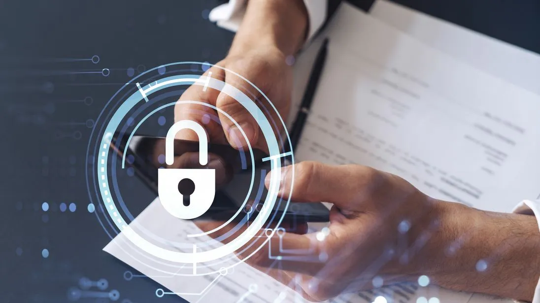 Ein Geschäftsmann in formeller Kleidung liest einen Vertrag, um Risiken im Bereich der Cybersicherheit vorzubeugen, und überprüft Details auf seinem Smartphone. Über dem Schreibtisch sind Hologramm-Symbole in Form von Vorhängeschlössern zu sehen.