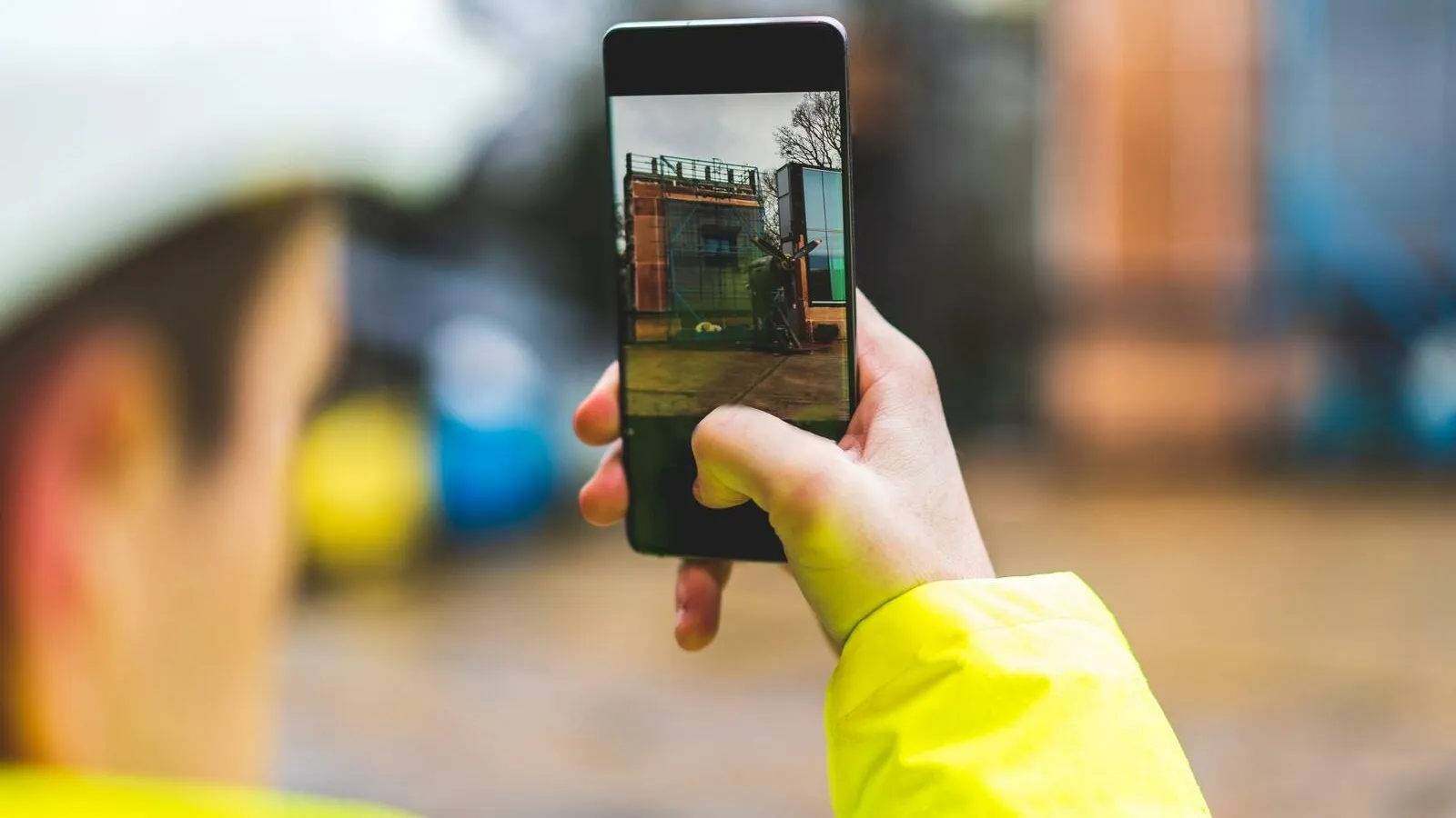 Ein Bauarbeiter hält sein Smartphone hoch, um ein Foto von der Baustelle zu machen.