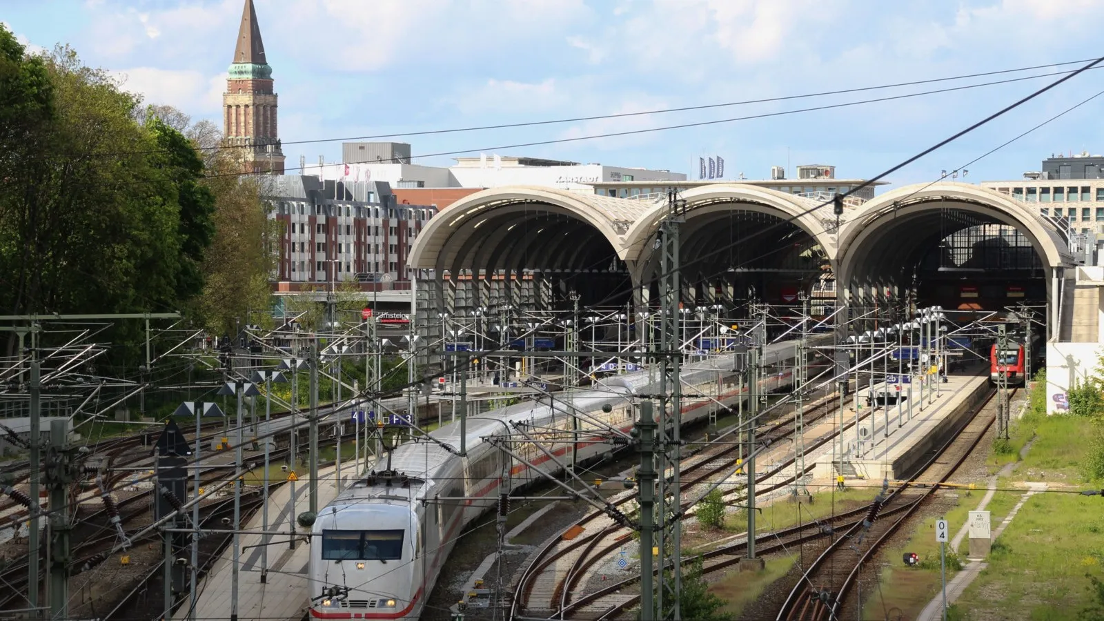 Vogelperspektive: Blick auf einen fahrenden Zug und den dahinter liegenden Hauptbahnhof.