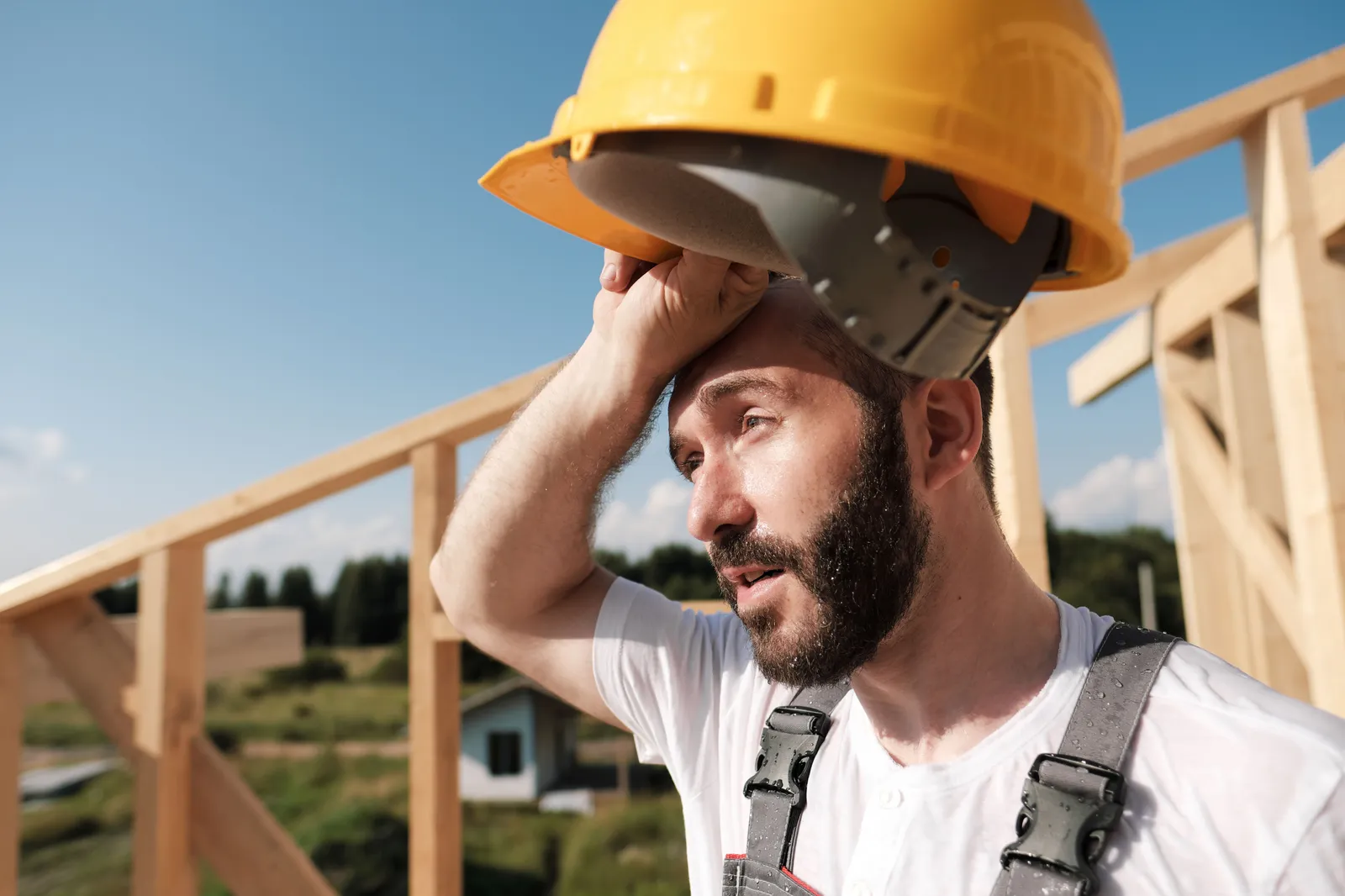 Ein Handwerker wischt sich mit dem Handrücken den Schweiß von der Stirn, er hat einen gelben Bauhelm in der Hand.